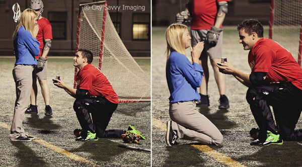 A man in athletic gear kneels on a sports field, holding a ring box for a surprise proposal to Megan. She looks surprised and happy as Chris pops the question, with other players cheering nearby.
