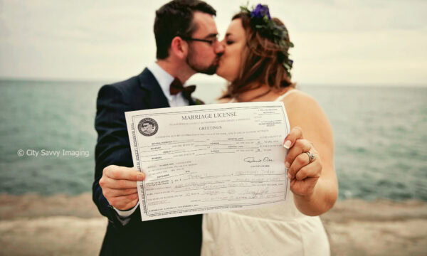 Ashley & Michael share a tender kiss, holding their marriage license in front of them, celebrating their intimate Museum Campus elopement by the shimmering water.
