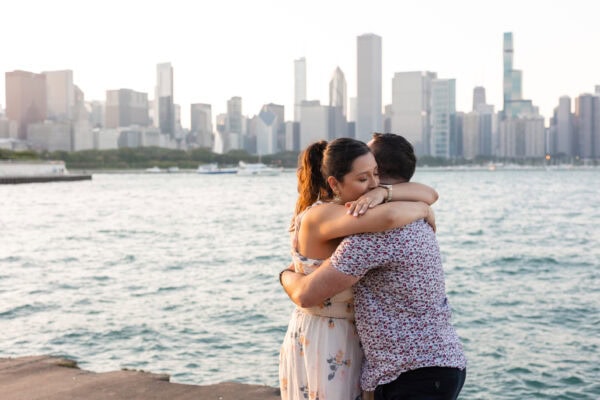 a couple celebrates their Surprise engagement sharing a hug in front of the chicago skyline at the adler planetarium