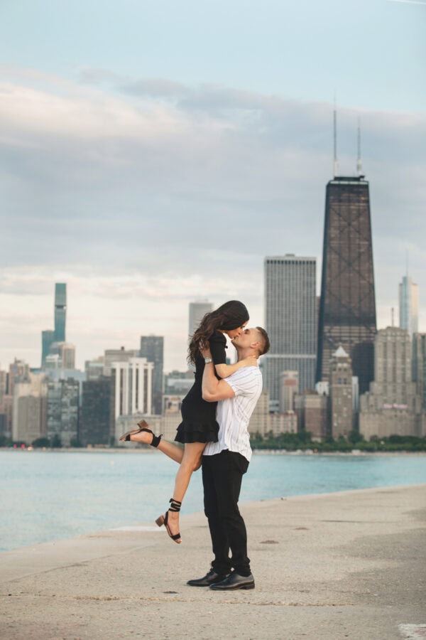 An engaged couple pose for a photo in front of the chicago skyline