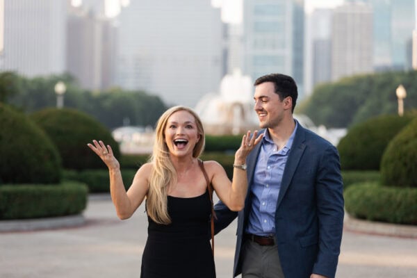 Woman celebrates in excitement after a surprise proposal as her partner smiles, with Chicago skyline in the background.