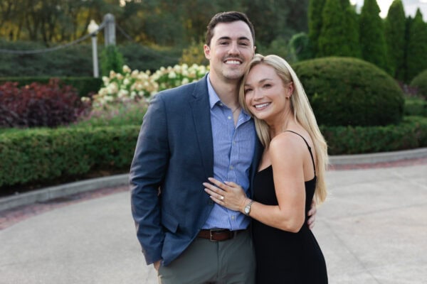 Newly engaged couple embracing in a garden setting, showing off an engagement ring after a joyful surprise proposal.
