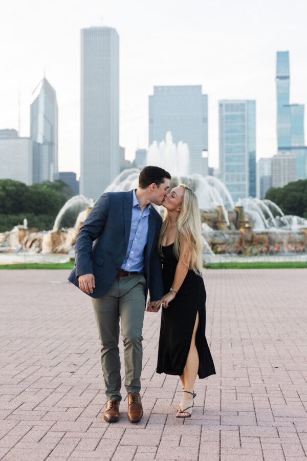 Engaged couple kisses while walking at buckingham fountain Chicago after their surprise proposal.