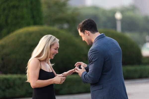 Man placing engagement ring on partner’s finger as she reacts with joy during a surprise proposal at grant park garden