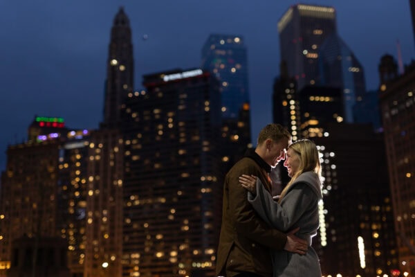 Newly engaged couple shares a romantic moment with Chicago's skyline glowing in the background at blue hour