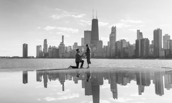 A man gets down on one knee to propose to his fiance in front of the chicago skyline