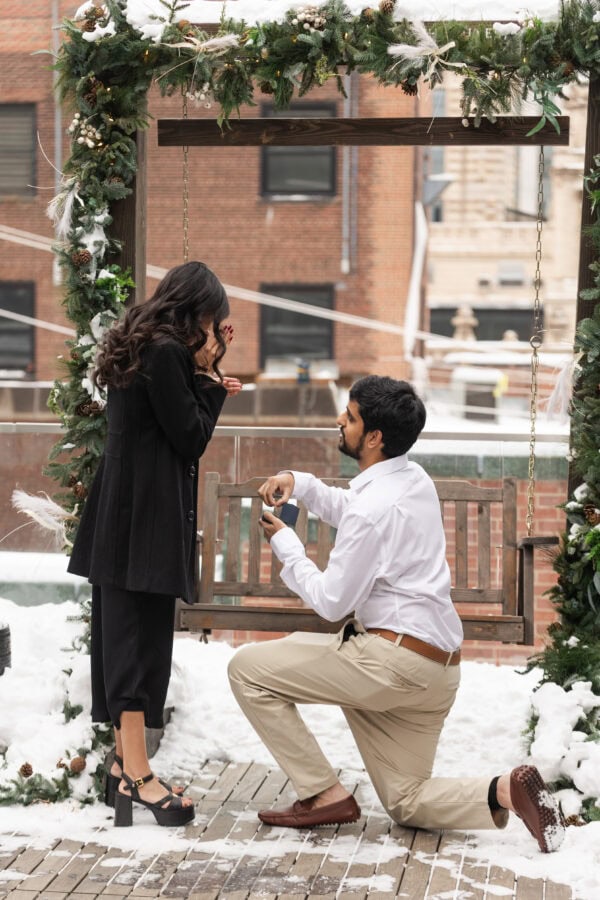 a man is on one knee proposing to his girlfriend on the rooftop of the Pendry in Chicago in the winter