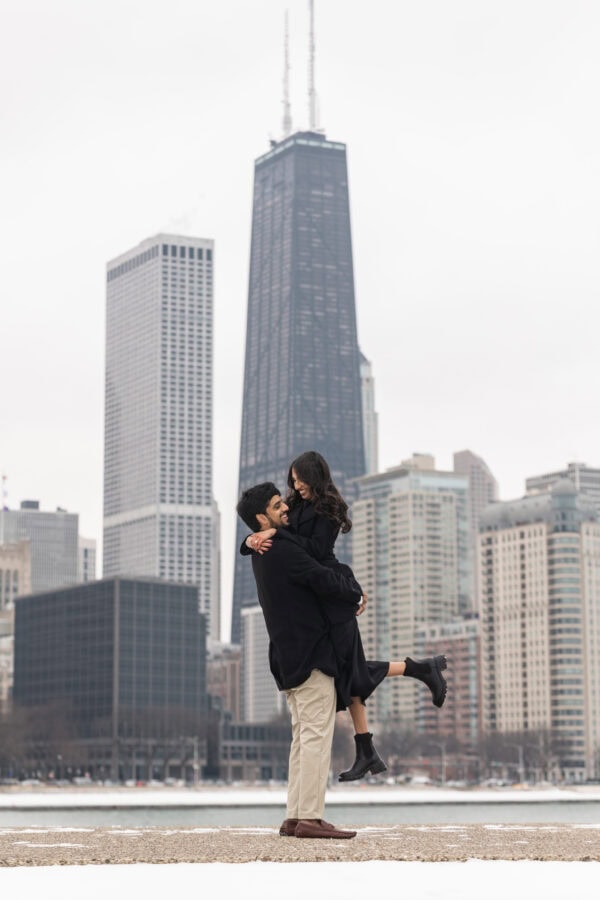 a couple posing for engagement photos at Olive Park in in front of the Chicago Skyline on a winter day