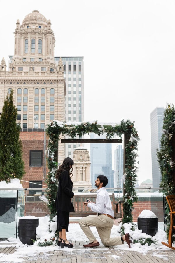 a man is on one knee proposing to his girlfriend on the rooftop of the Pendry in Chicago in the winter