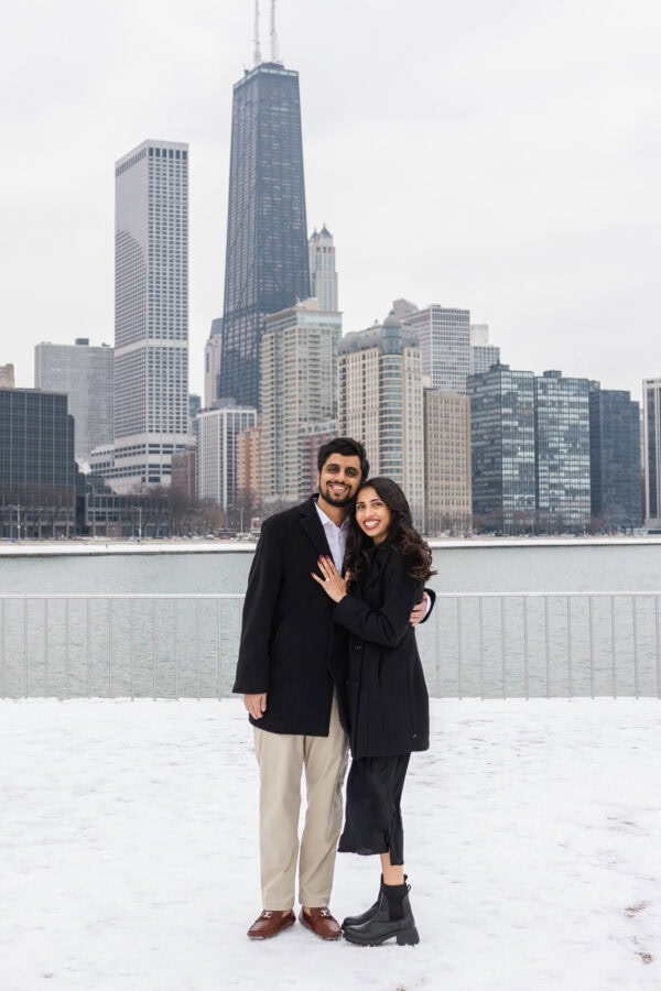 a couple posing for engagement photos at Olive Park in in front of the Chicago Skyline on a winter day