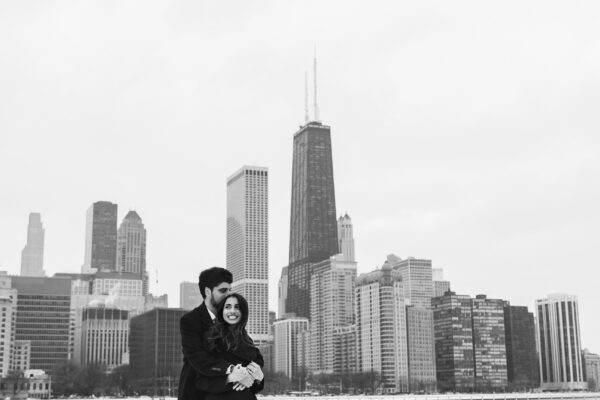 a couple posing for engagement photos at Olive Park in in front of the Chicago Skyline on a winter day