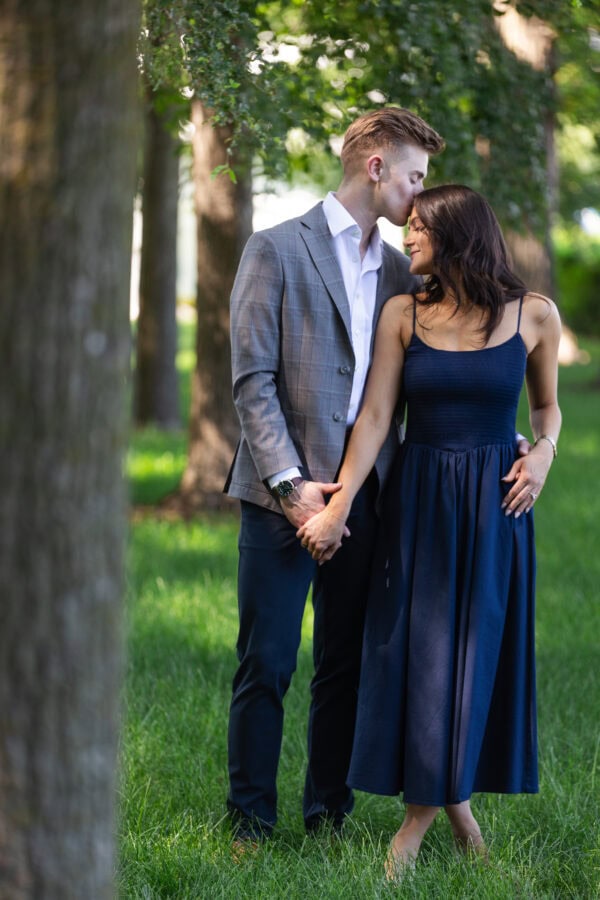 a man kisses his girlfriend on the forehead while holding her hand