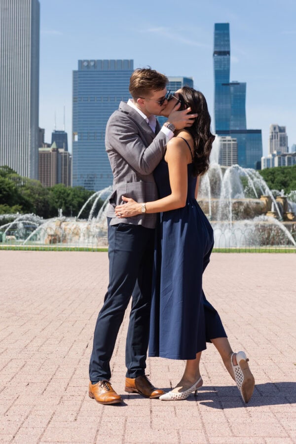 a man and women both in sunglasses stop for a kiss in front of the chicago buckingham fountain