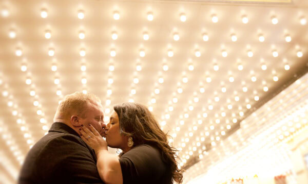 Ashley and Steve share a tender kiss under the brightly lit marquee, the numerous lights in the background adding a magical touch to their engagement session.