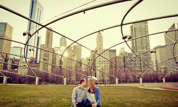 Jill & Drew share a kiss on a bench in Millennium Park, framed by modern architecture and towering skyscrapers during their enchanting engagement session.