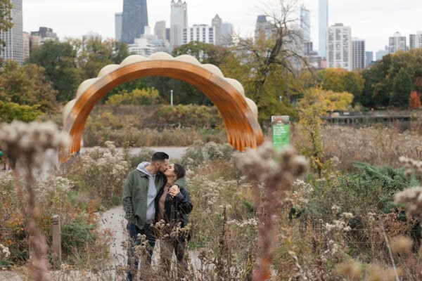 A newly engaged couple shares a kiss in front of the chicago skyline in Lincoln Park