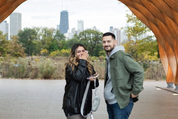 a couple shares a look of shock after the groom to be proposed to his partner in front of the chicago skyline