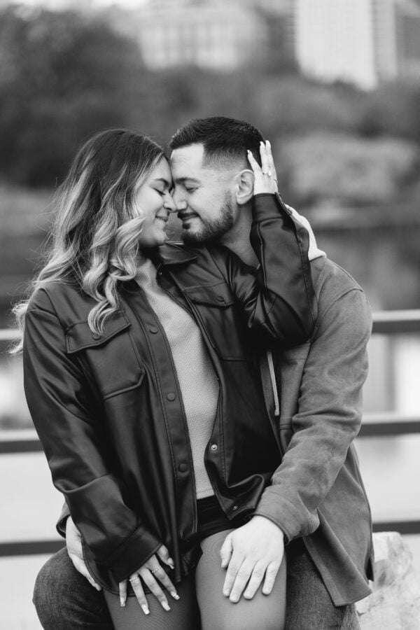 A newly engaged couple poses for a photo sitting on a rock in black and white