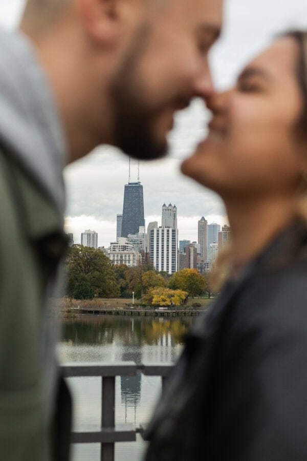 A newly engaged couple touches noses out of focus with a clearly focused Chicago skyline behind them