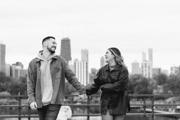 A newly engaged couple walks and laughs while in front of the chicago skyline in Lincoln Park