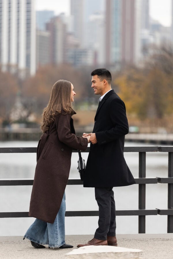 Couple holding hands with Chicago skyline behind them just before he proposes to her.