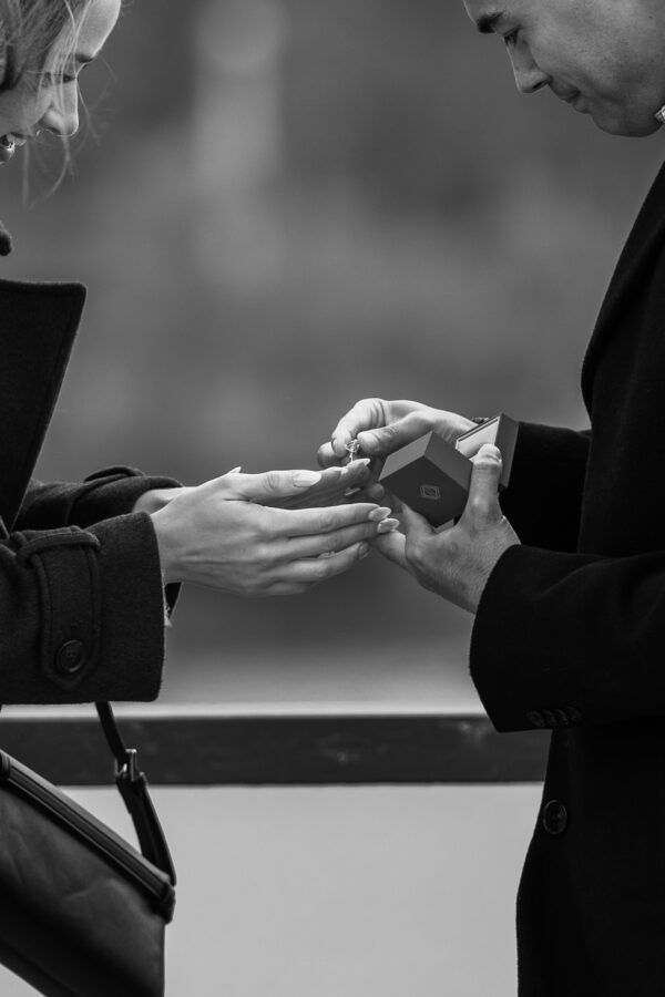 Man puts an engagement ring on his partners hand with Chicago skyline behind them during a surprise proposal