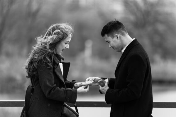 Man puts an engagement ring on his partners hand with Chicago skyline behind them during a surprise proposal