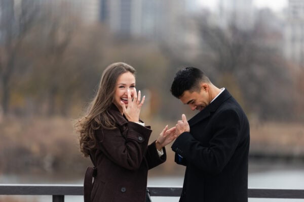 Couple holds hands and celebrates with Chicago skyline behind them during a surprise proposal