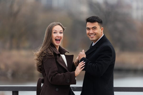 couple discovers the camera as she screams with joy with Chicago skyline behind them during a surprise proposal