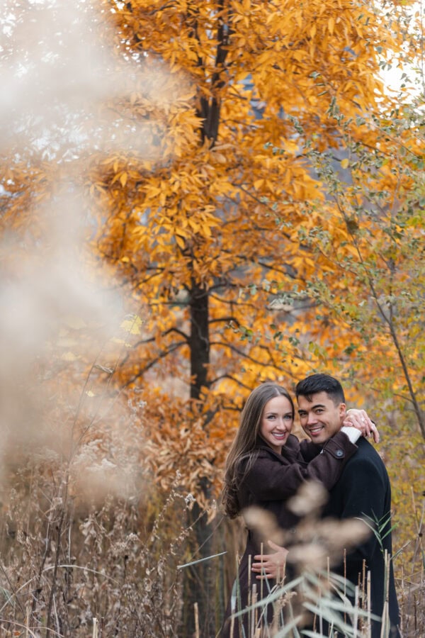 Couple poses for a photo during an engagement session with orange fall leaves behind them