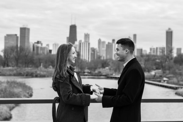 Couple holds hands and celebrates with Chicago skyline behind them during a surprise proposal