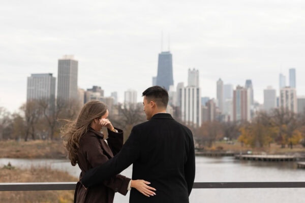 Couple stands with Chicago skyline behind them after a surprise proposal as she wipes a tear away