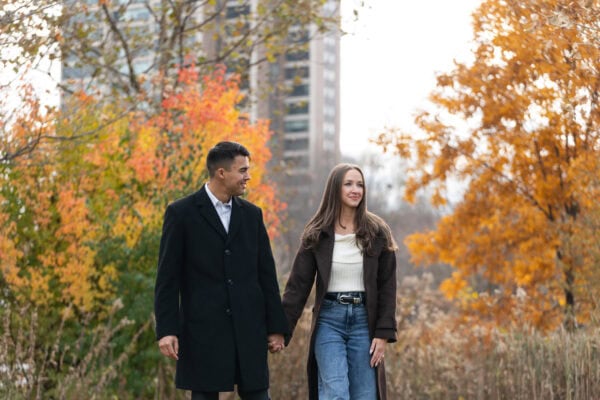 Couple poses for a photo during an engagement session with orange fall leaves behind them