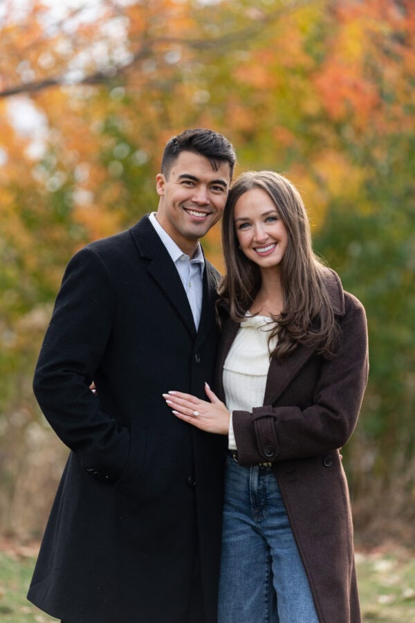 Couple poses for a photo during an engagement session with orange fall leaves behind them