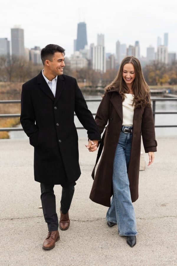 Couple holding hands and walking in front of the Chicago skyline behind them during an engagement session