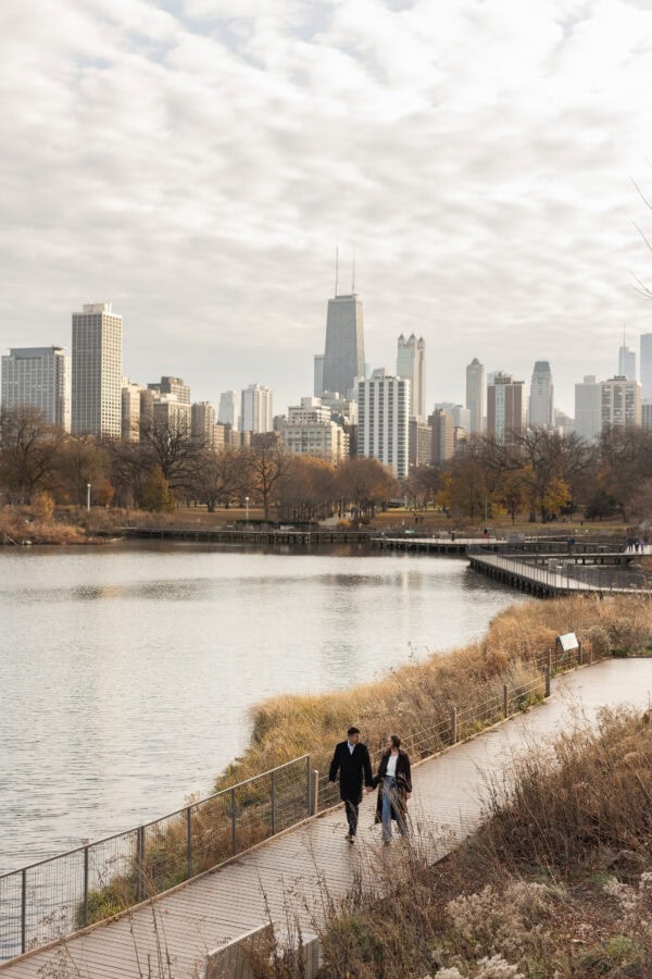 Couple holding hands and walking in front of the Chicago skyline behind them during an engagement session