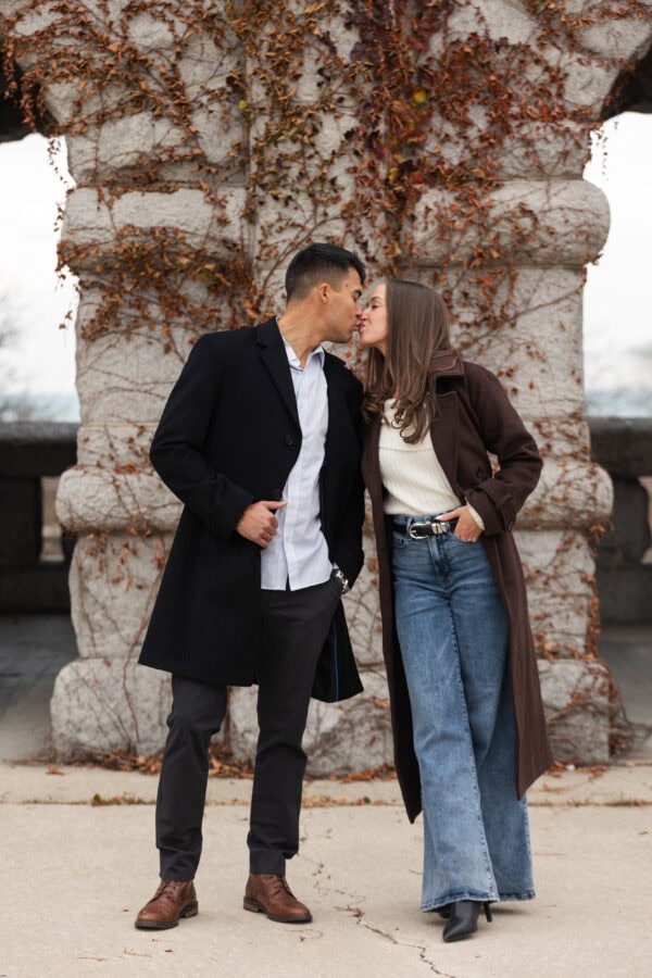 Couple poses for a photo during an engagement session in front of an ivy covered stone building