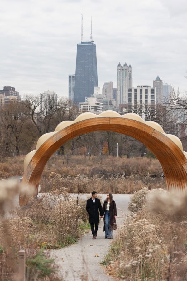 Couple holding hands and walking in front of the Chicago skyline behind them during an engagement session