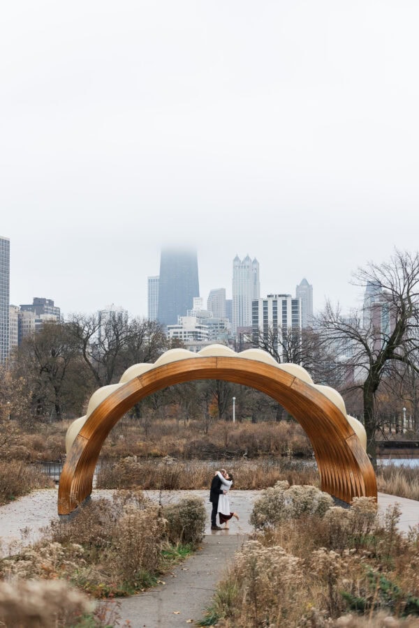 a couple poses for an engagement photo as they share a kiss under a pavilion in Chicago's lincoln park zoo
