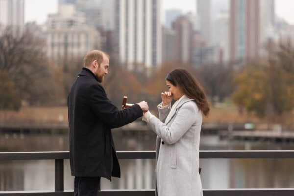 a man puts an engagement ring on the finger of his new fiance as she wipes a tear off her face.