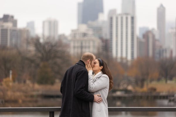 a newly engaged couple shares a celebratory kiss in front of the chicago skyline