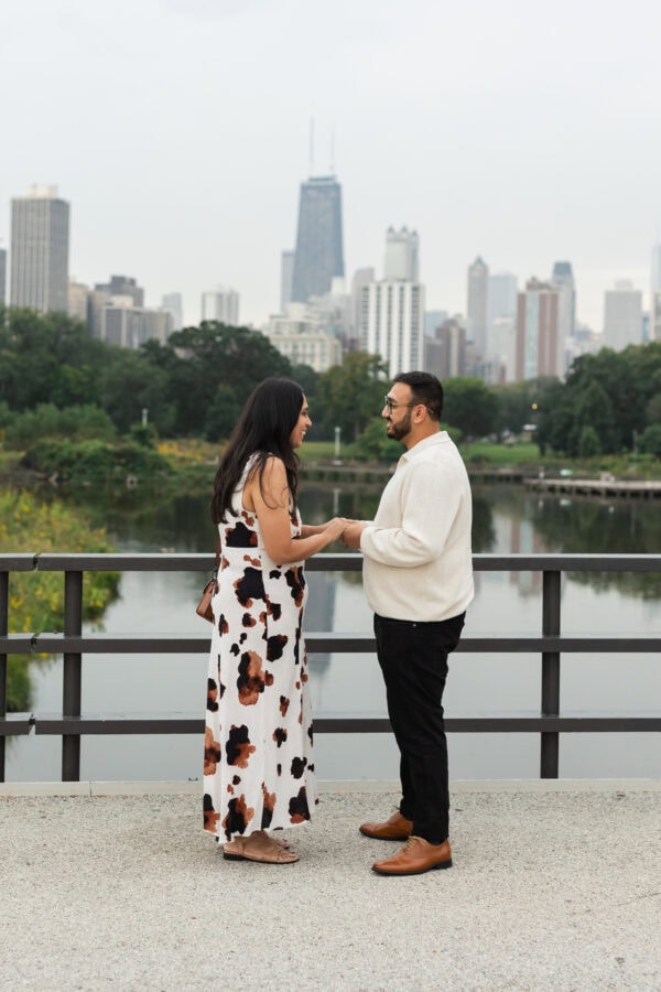 a man holds hands with his girlfriend in front of the chicago skyline at the Lincoln Park Zoo jus moments before proposing to her