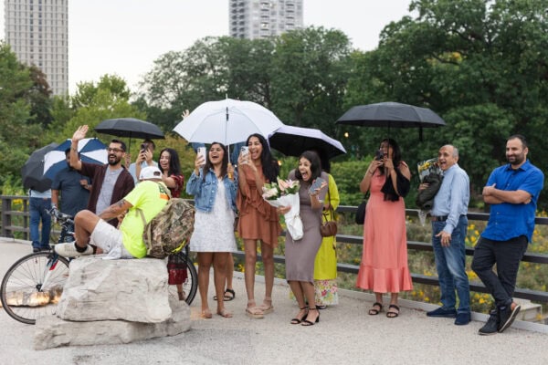 friends and family hold umbrellas in the rain as they cheer for a couple getting engaged