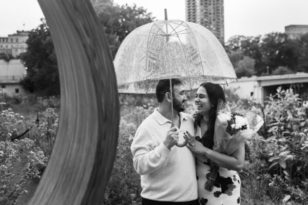 a newly engaged couple poses for a photo under an umbrella in the rain at lincoln park zoo