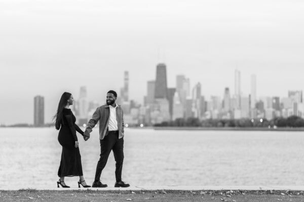 a newly engaged couple walks in front of the skyline in Chicago at the lakefront at montrose harbor