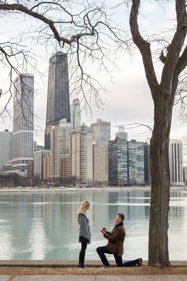 Romantic Chicago proposal as a man presents an engagement ring while kneeling by Lake Michigan.