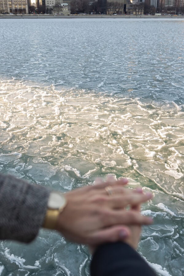 Close-up of blurred hands intertwined with engagement ring , lake water with ice in focus in background after a Chicago proposal