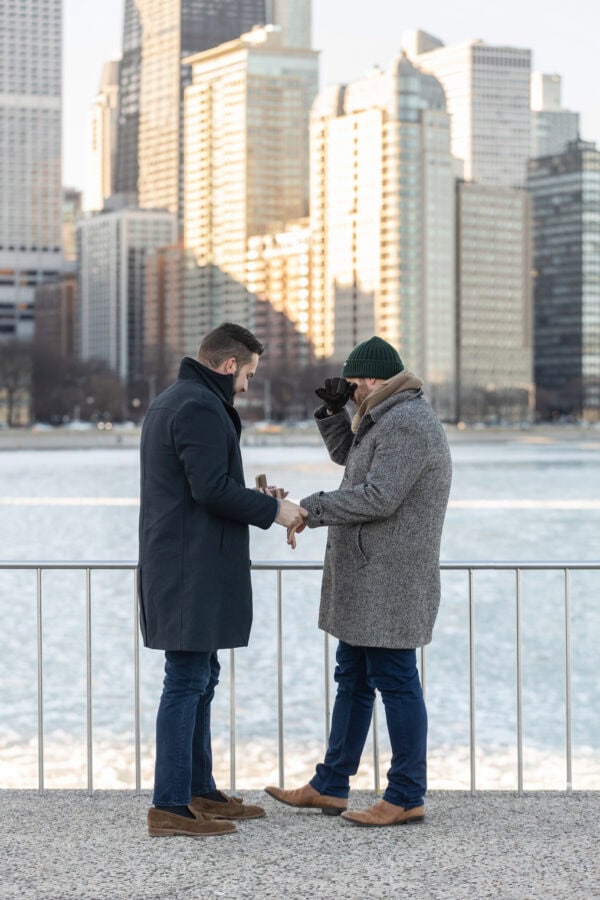 Man places engagement ring on partner’s finger by the lake as Chicago skyline glows in the background during a surprise proposal