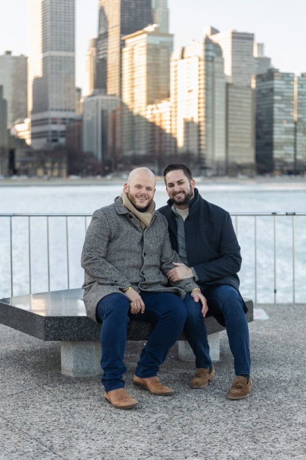 Couple sitting together by the lake with Chicago skyline behind them, posing for an engagement photo