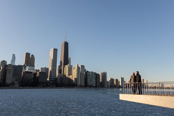 Couple holding hands by the lake with Chicago skyline behind them, posing for an engagement photo at Olive Park